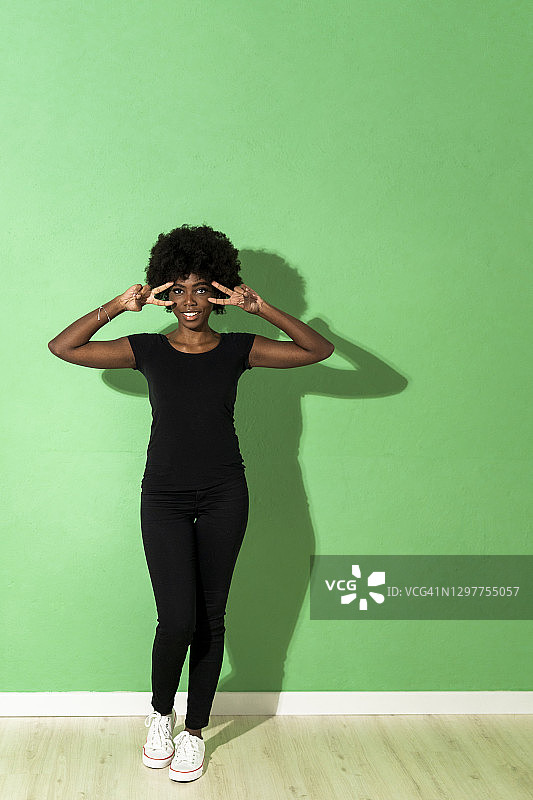 年轻女子站在绿色背景下，做着和平手势图片素材