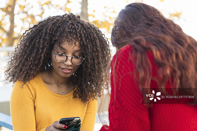 微笑的非洲女人和女朋友在公园使用手机图片素材