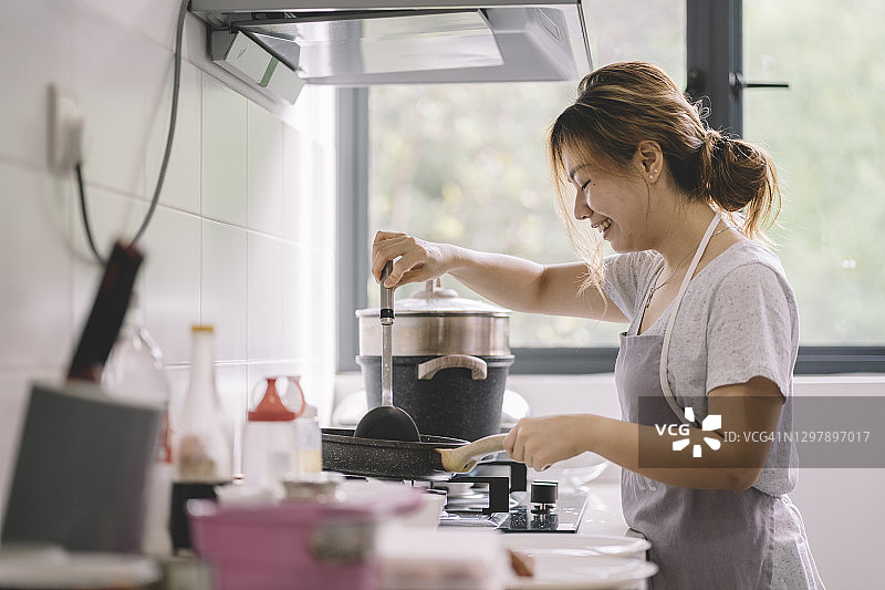微笑的亚洲中国女人在厨房做饭图片素材