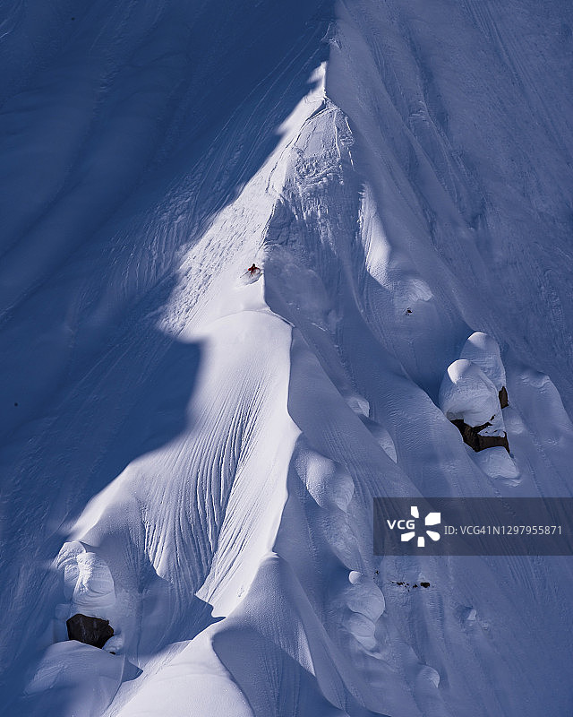 远处的滑雪者下了陡峭的雪脊线图片素材