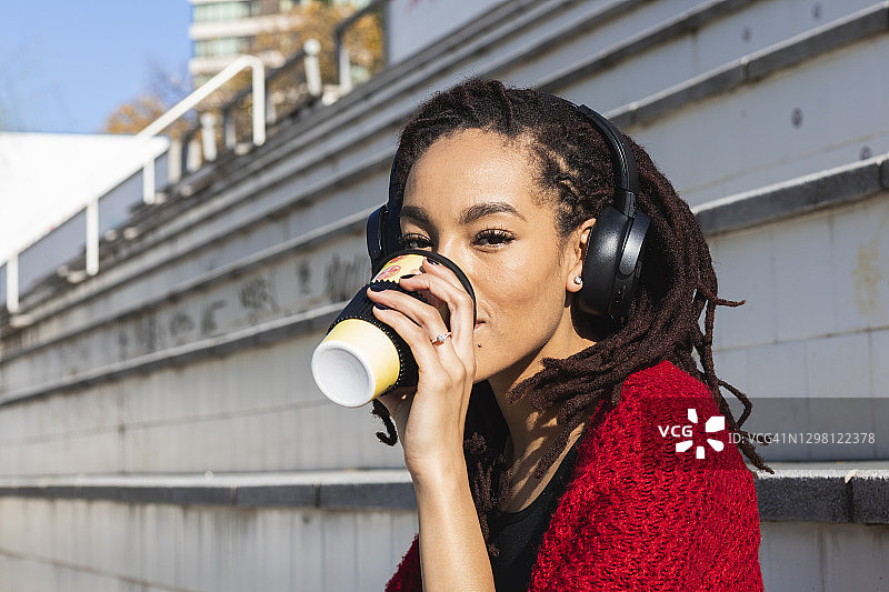 在阳光明媚的日子里，年轻女子一边听音乐，一边用可重复使用的杯子喝咖啡图片素材