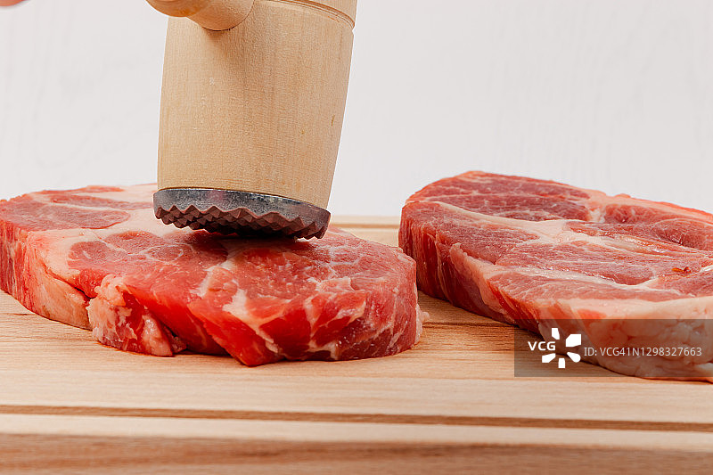 新鲜的生牛排放在厨房砧板上，白色的木桌上。在他们的上方是一个打肉的锤子图片素材