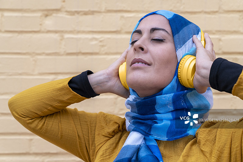 穆斯林妇女使用无线耳机听音乐图片素材
