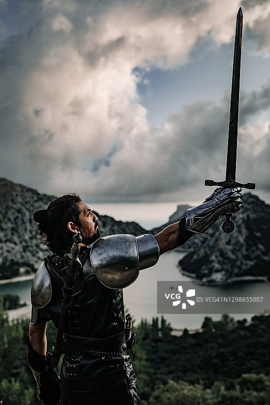 黑色的中世纪幻想骑士在一个惊人的风景和戏剧性的天空举起他的剑图片素材