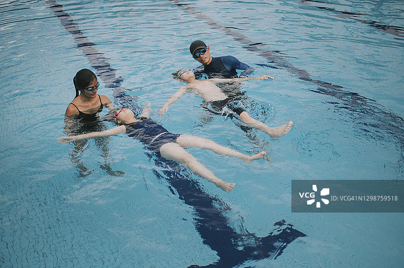 2名亚洲华人教练指导他们的年轻学生在游泳池的水面上漂浮图片素材
