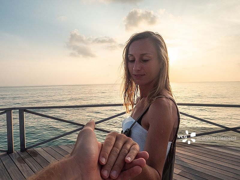 一对夫妇在日落时在木制码头上牵手，热带度假图片素材