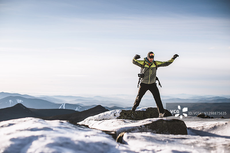 冬天，一个带着相机的人从山顶的冰岩上跳下来图片素材