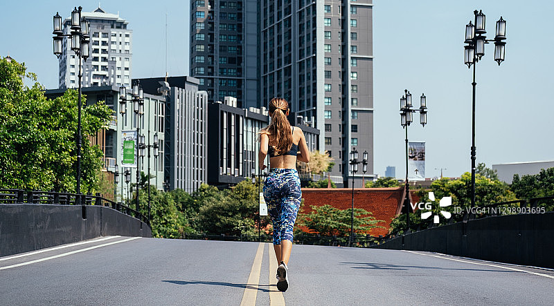 女人在城市道路上奔跑的后视图与建筑物的背景图片素材