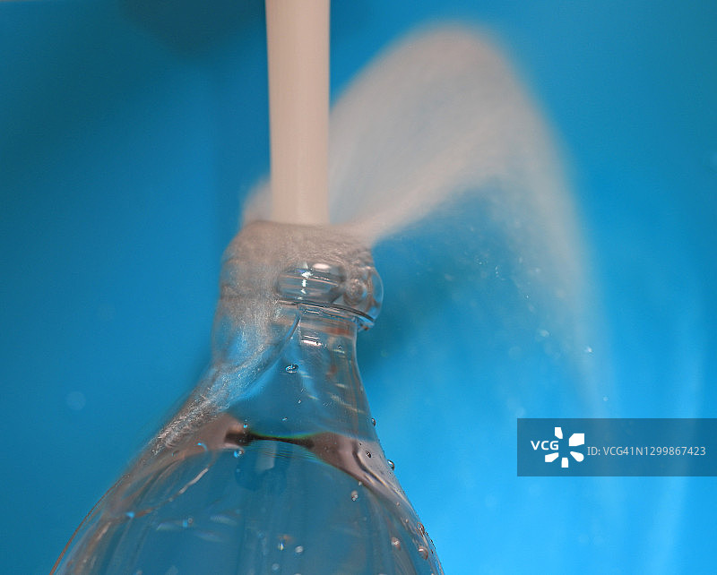 蓝色背景下，清水从水龙头流出溢满塑料瓶图片素材