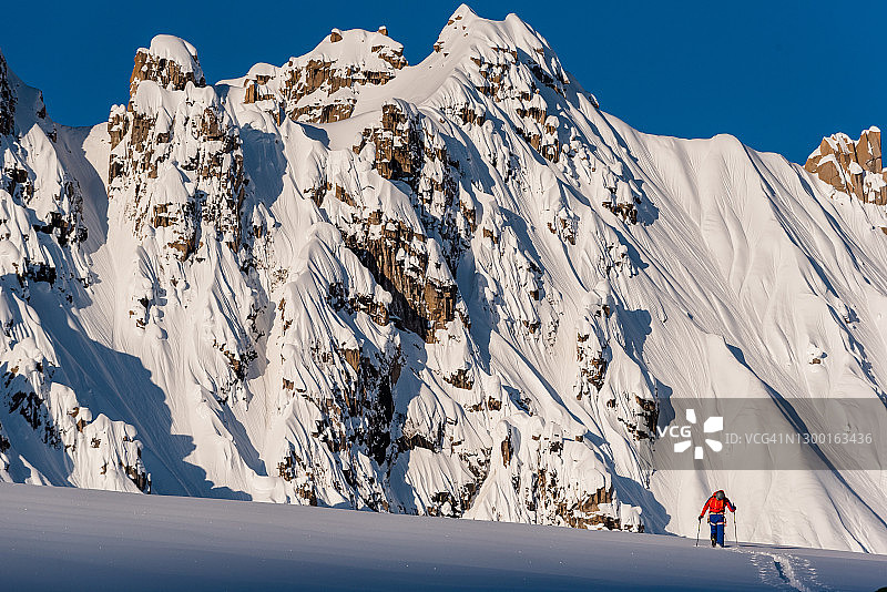 滑雪登山运动员在高耸的山脉下攀登雪坡图片素材