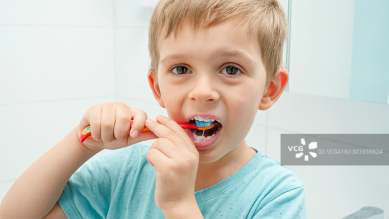 一个蹒跚学步的小男孩在早上刷牙时照镜子的肖像。儿童卫生和保健图片素材