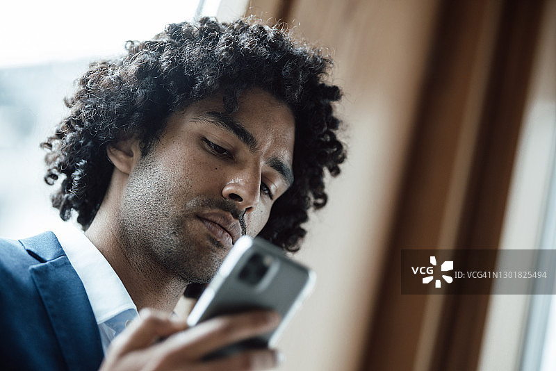 一头黑色卷发的年轻男性企业家在办公室使用智能手机图片素材