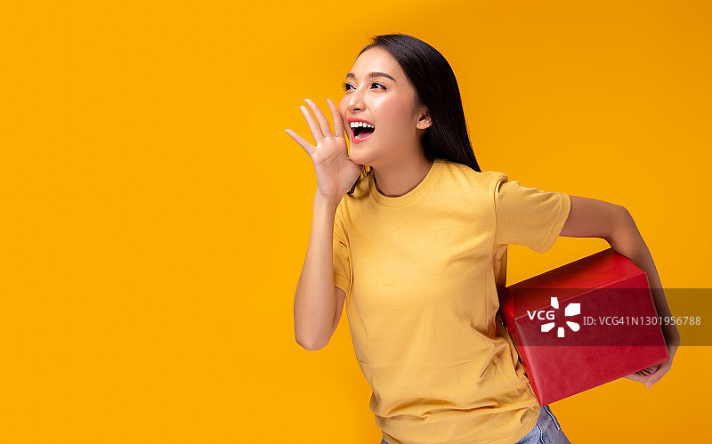 快乐年轻的亚洲女人拿着礼盒和宣布复制空间，站在黄色的背景美丽的亚洲女孩快乐微笑持有新年礼盒礼品享受女性使用的广告图片素材