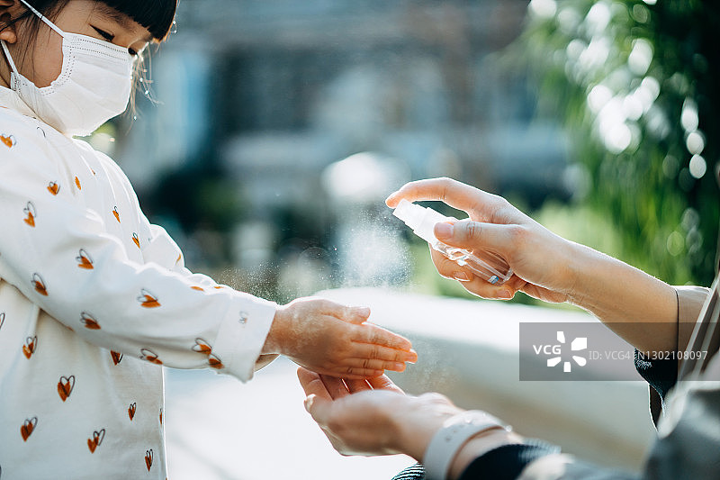 年轻的亚洲母亲喷洒洗手液到小女儿的手在一个公园的户外，以保护和防止病毒在城市的传播。保持个人卫生。日常生活的新常态图片素材