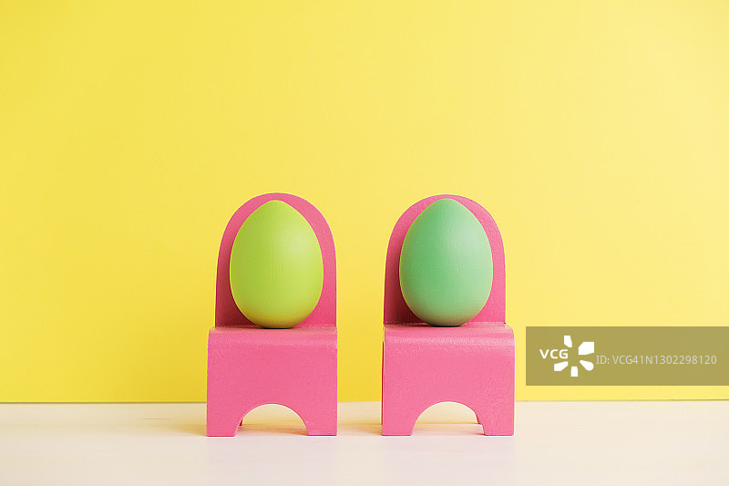 复活节节日概念用可爱的蛋生活。不同的情绪和感受。一对可爱的鸡蛋坐在黄色背景的粉红色椅子上图片素材
