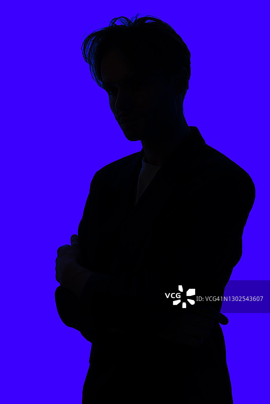 一个年轻人的剪影穿着时髦的夹克站在蓝色发光的背景图片素材