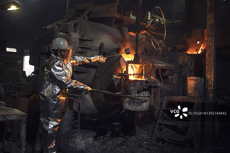 消防服和安全帽工人控制铸造炉炼铁过程。图片素材