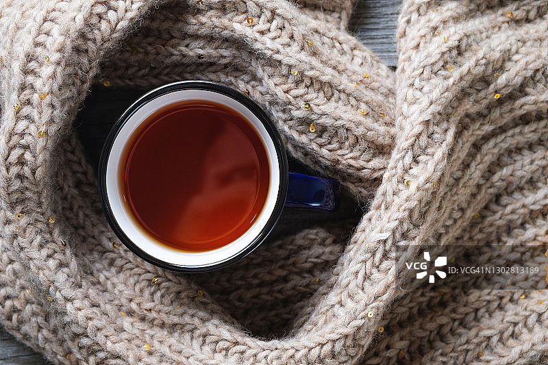 热咖啡或茶在一个杯子，温暖舒适的针织羊毛围巾，背景是一个旧的木制背景或桌子。季节性放松的概念，放松心灵的平和。图片素材