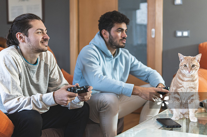 年轻的男性朋友们坐在家里的桌子上玩电子游戏图片素材