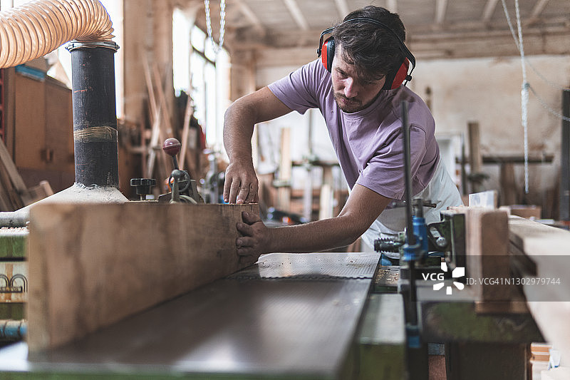 年轻男性工匠在车间工作时手持木板在工作台上工作图片素材