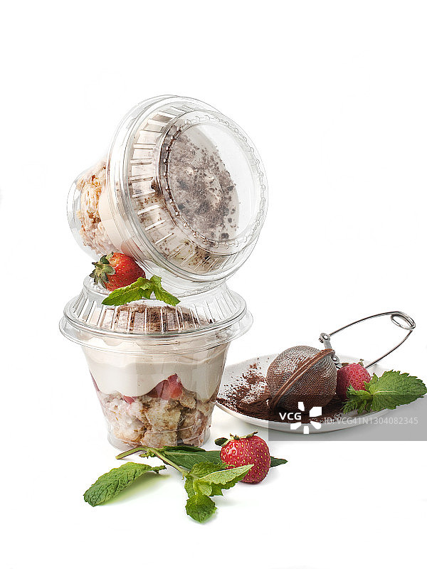 食物摄影饼干和酸奶分层甜点与巧克力和可可粉近距离在一个封闭的塑料杯交付，侧面的白色背景孤立图片素材