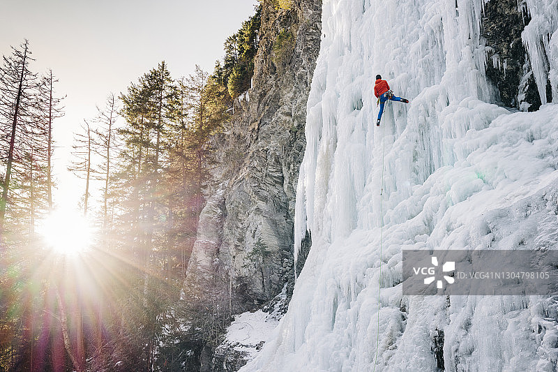 明亮的日出与冰上攀登者上升一个高大的冰冻瀑布，太阳在地平线上的顶峰图片素材