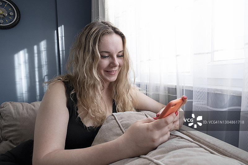 快乐的年轻女子在家里的沙发上使用手机图片素材