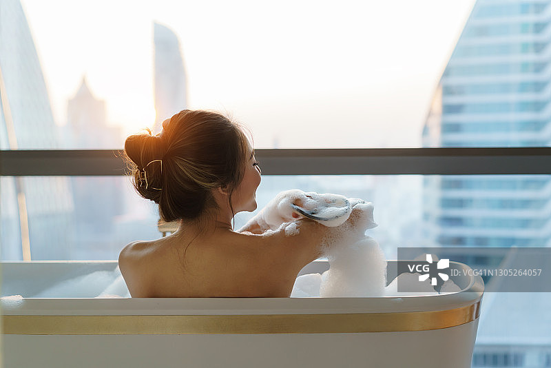 一名亚洲女子度假时在市中心豪华酒店浴室的浴缸里用肥皂泡洗澡。图片素材