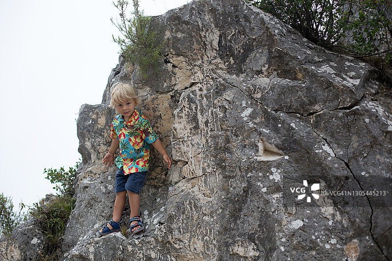 孩子，金发的蹒跚学步的男孩，站在山上的一块大石头上，微笑着图片素材