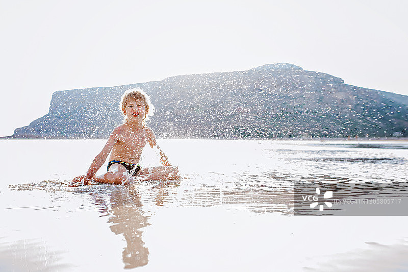 一个男孩在海滩上戏水。巴洛斯海滩和天堂岛在克里特岛，希腊-库存照片图片素材