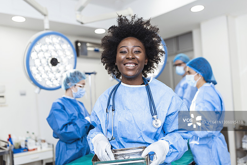 笑容可掬的非裔美国女外科医生在手术室里穿着外科制服拿着手术器械的肖像。在医院手术室的年轻女医生图片素材
