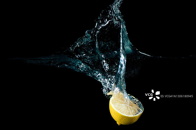 在黑色背景下，将一半的柠檬放入水中图片素材