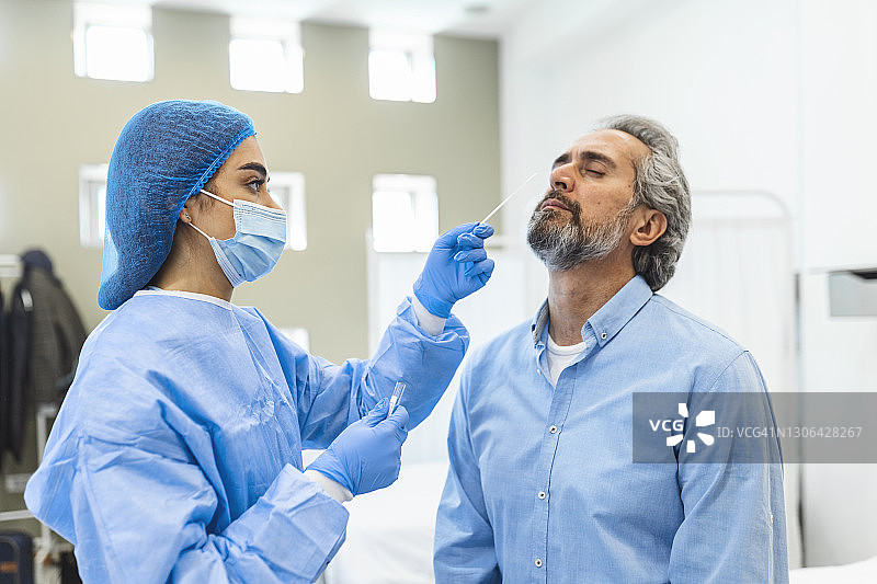 医护人员使用防护设备对老人进行冠状病毒拭子。鼻拭子检测Covid-19。图片素材