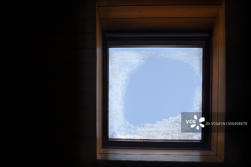 雪在一个内部天窗的玻璃上，映衬着清澈的蓝色天空，从下面直接拍摄图片素材