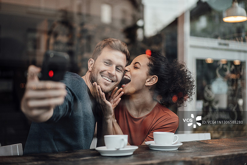 微笑的男友与女友坐在咖啡厅用手机自拍图片素材