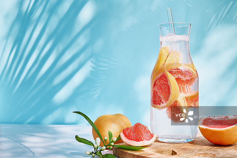 柚子，迷迭香，多汁的柑橘类水果。新鲜健康的葡萄柚饮料在阳光与阴影。创意饮料在蓝色柔和的背景。图片素材