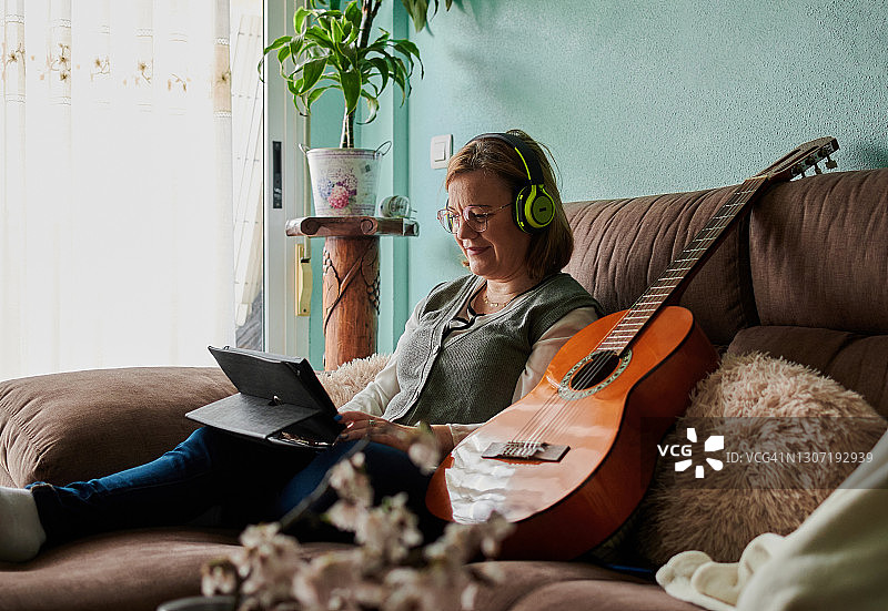 中年妇女戴着耳机在家学习弹吉他图片素材