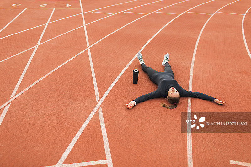 一名疲惫绝望的女子在经过艰苦的训练后躺在体育场的跑道上图片素材