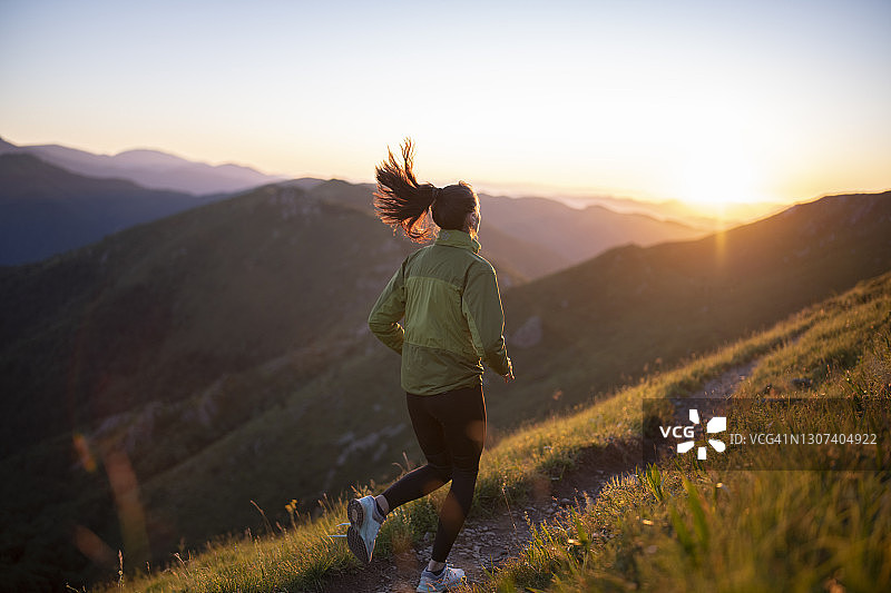 一个健康的女人在日落时分在山上慢跑。图片素材