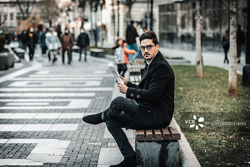 一个年轻的商人坐在城市的长椅上读金融报纸的侧视图图片素材