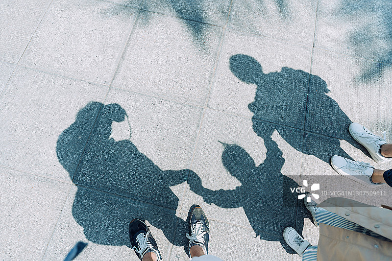 在一个阳光明媚的日子里，一个充满爱的三口之家手牵着手在户外散步图片素材