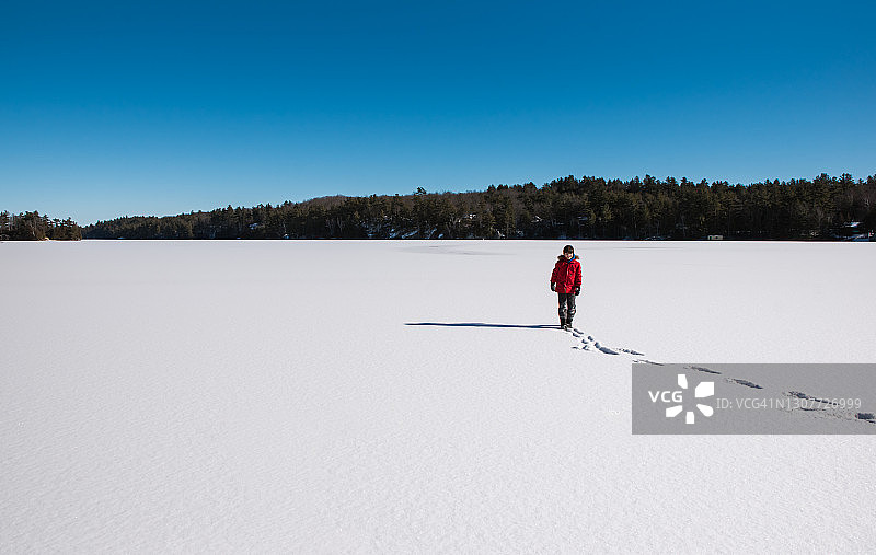 一个小男孩独自站在结冰的湖面上。图片素材