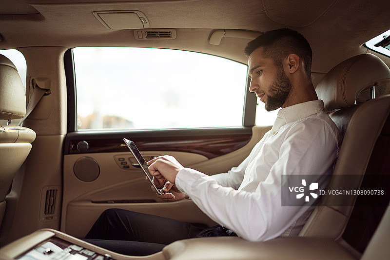 一名男子坐在汽车后座上使用平板电脑图片素材