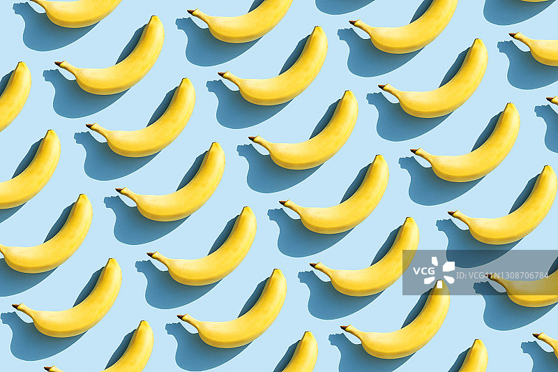 鲜艳的水果图案的新鲜黄色香蕉在蓝色的背景与阴影。水果的概念。平躺，俯视图。图片素材