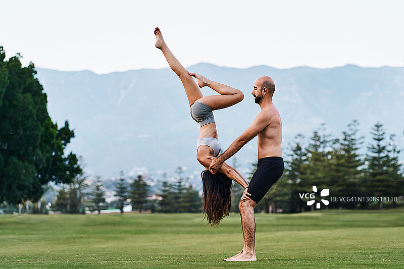 一对情侣在公园里一起做瑜伽倒立图片素材