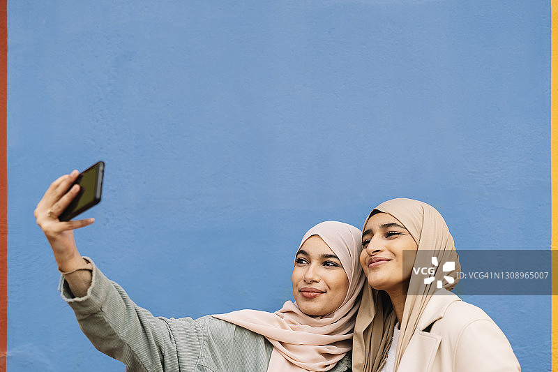 两位阿拉伯女性朋友正在用智能手机自拍。图片素材