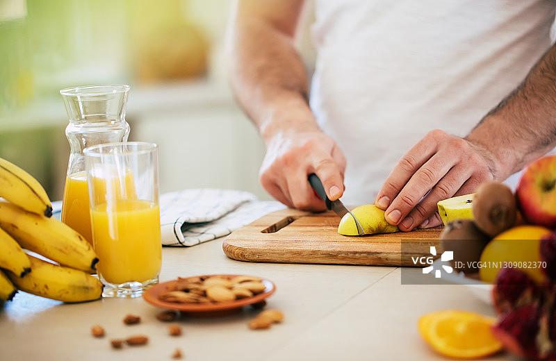 英俊的年轻运动微笑的男人在厨房准备素食健康的水果沙拉和冰沙在一个好心情图片素材