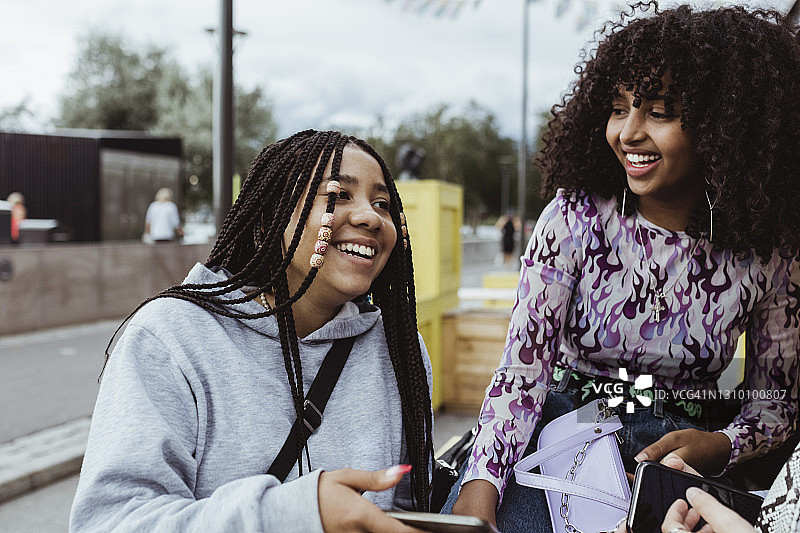 女青少年女性朋友笑着与智能手机在人行道上图片素材