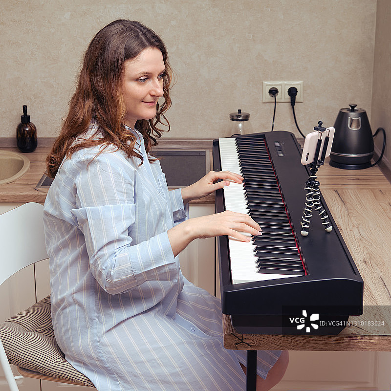 一个穿着蓝色睡衣的孕妇在弹钢琴。家庭厨房音乐课关闭图片素材