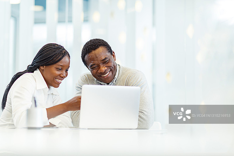快乐的非裔美国商业同事在办公室用笔记本电脑工作。图片素材